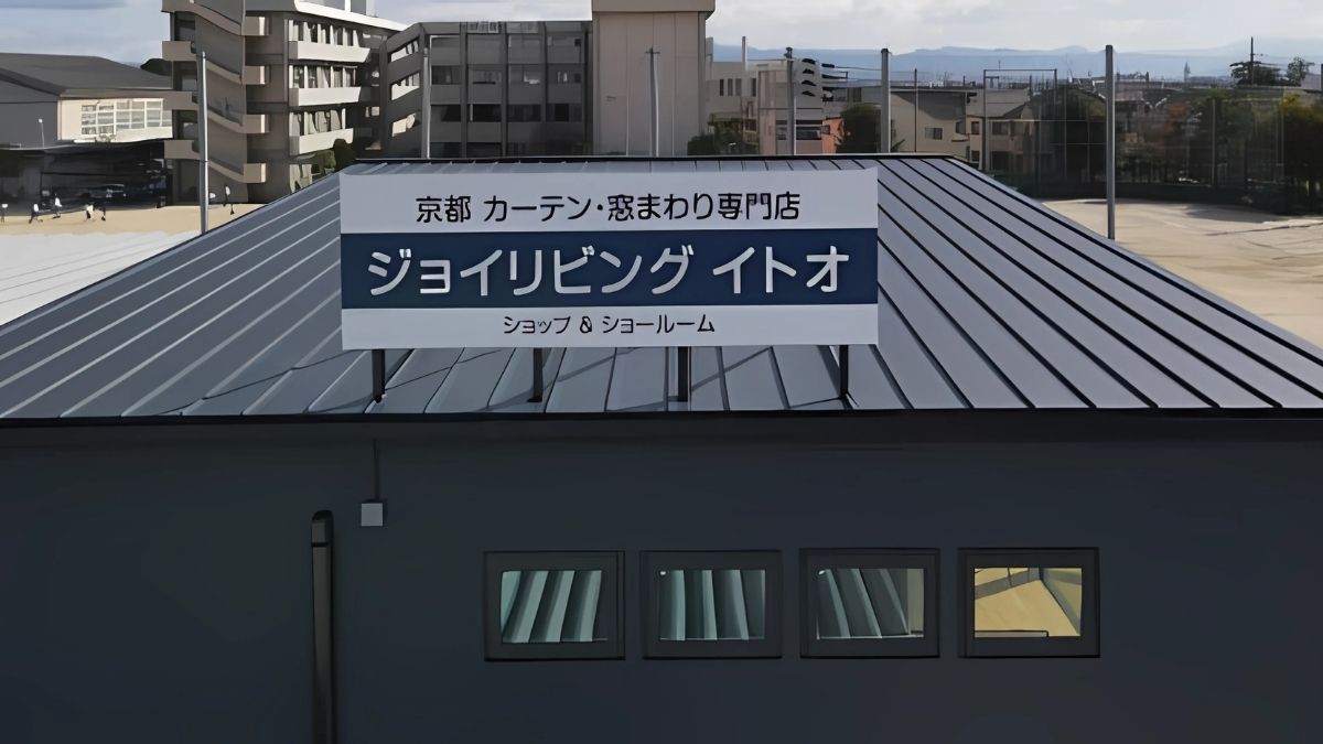 ジョイリビングイトオの社屋に取り付けられた看板。奥に中学校のグランドが見えている